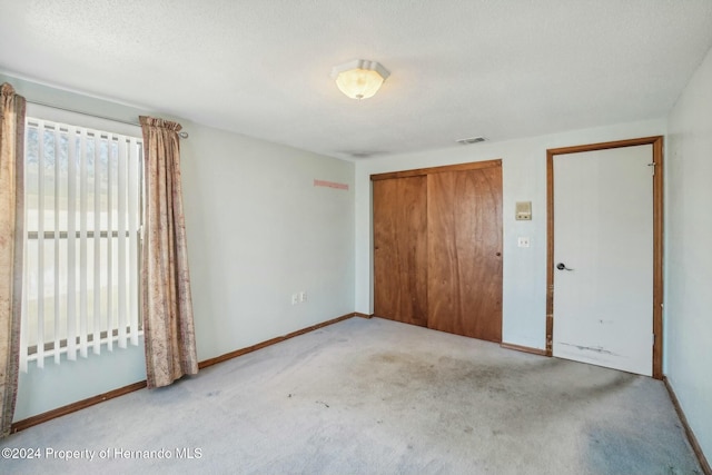 unfurnished bedroom with light carpet, a closet, and a textured ceiling