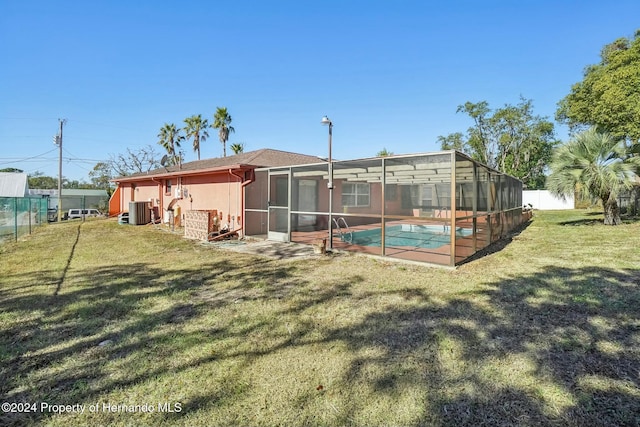 rear view of property featuring a fenced in pool, a yard, central air condition unit, and glass enclosure