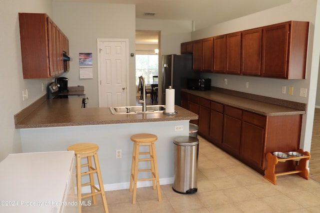 kitchen featuring stainless steel refrigerator, sink, kitchen peninsula, a breakfast bar area, and range