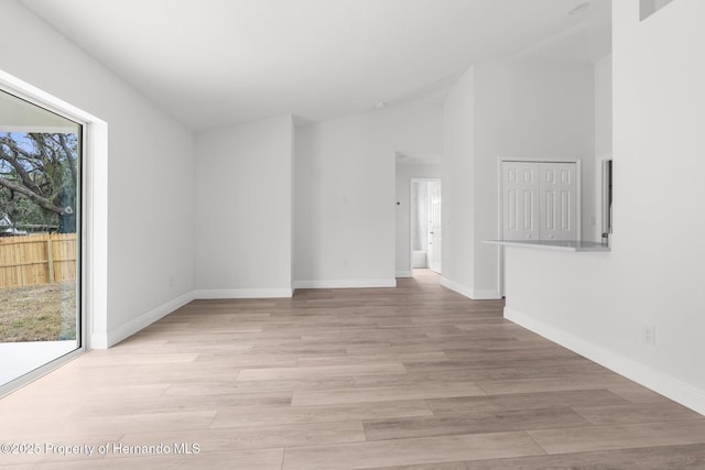 empty room with light wood-style floors, baseboards, and vaulted ceiling