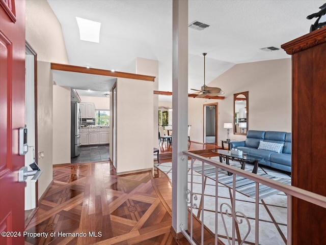 foyer with ceiling fan, vaulted ceiling with skylight, dark parquet floors, and a textured ceiling