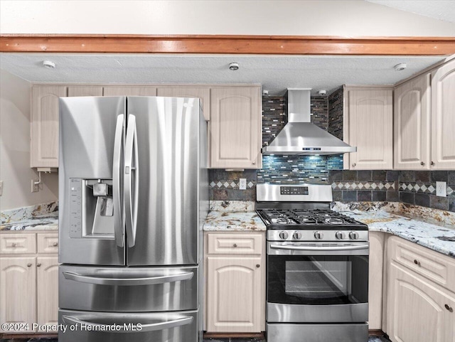 kitchen featuring wall chimney range hood, tasteful backsplash, light stone counters, a textured ceiling, and appliances with stainless steel finishes