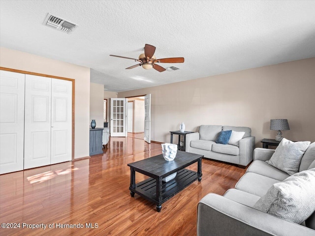 living room with hardwood / wood-style flooring, ceiling fan, and a textured ceiling