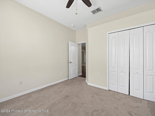 unfurnished bedroom with ceiling fan, a closet, light carpet, and a textured ceiling