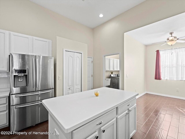 kitchen featuring dark wood-type flooring, washing machine and dryer, white cabinets, stainless steel fridge, and a kitchen island