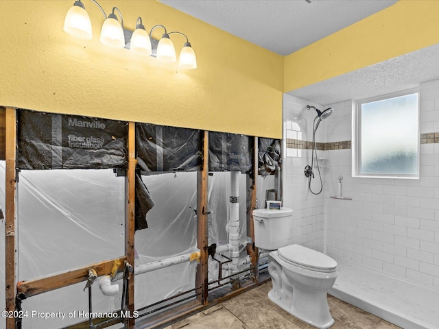 bathroom with tile patterned floors, toilet, a textured ceiling, and tiled shower