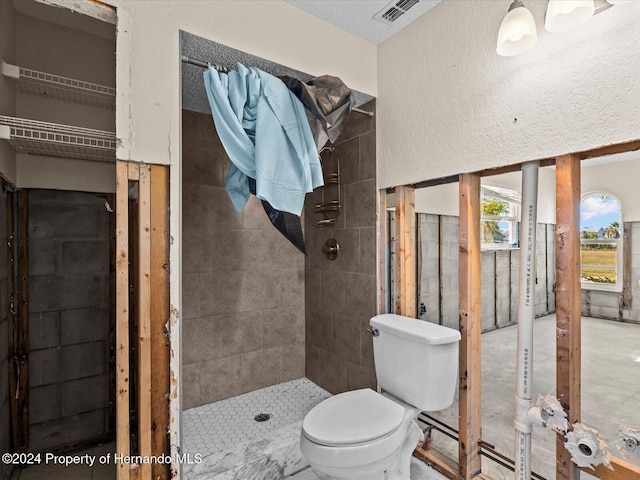 bathroom featuring tiled shower, a textured ceiling, and toilet