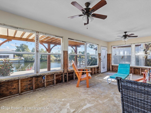 sunroom with ceiling fan and a water view