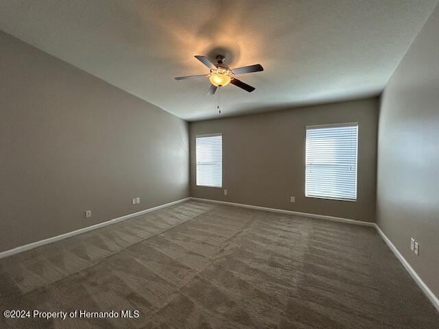 spare room with dark colored carpet and ceiling fan