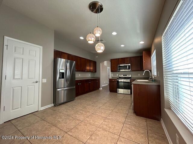 kitchen with sink, vaulted ceiling, decorative light fixtures, light tile patterned flooring, and appliances with stainless steel finishes