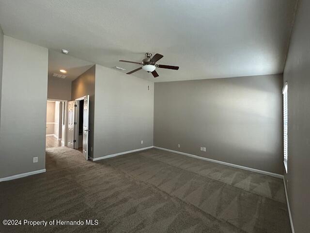 unfurnished room featuring dark carpet, ceiling fan, and lofted ceiling