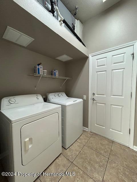 clothes washing area with washer and clothes dryer, light tile patterned flooring, and a textured ceiling