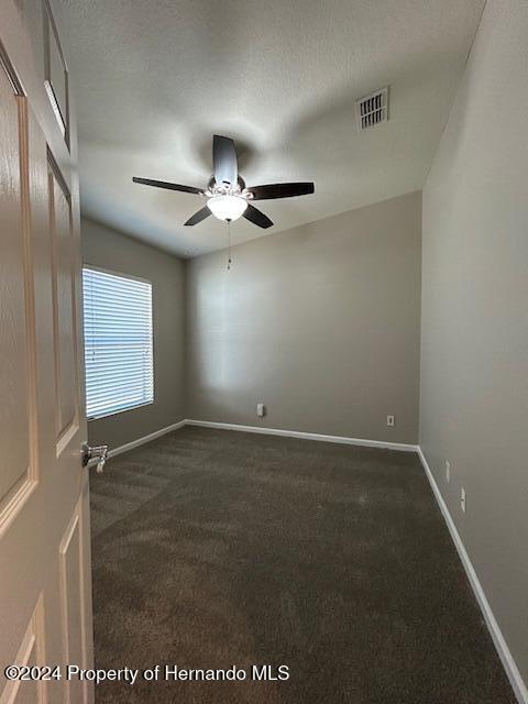 empty room featuring ceiling fan, a textured ceiling, and dark colored carpet