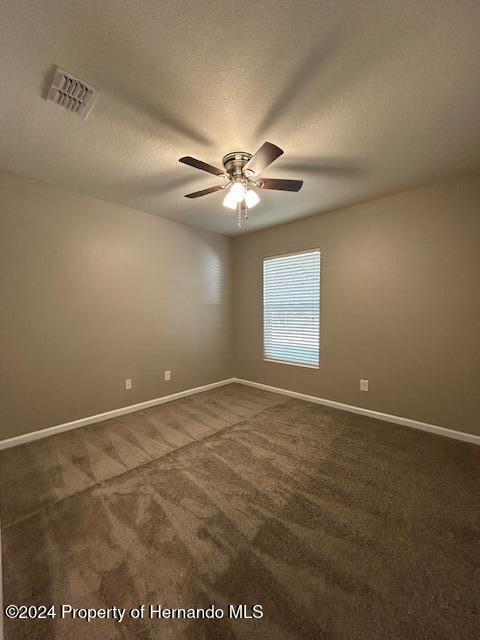 empty room featuring dark colored carpet, ceiling fan, and a textured ceiling