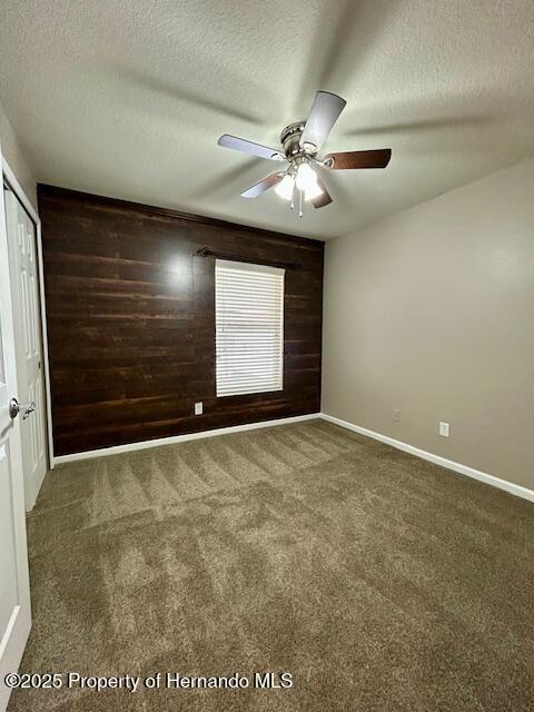 unfurnished bedroom with a textured ceiling, carpet floors, wood walls, and a closet