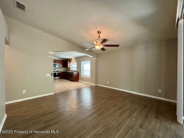 unfurnished living room with visible vents, arched walkways, a ceiling fan, baseboards, and wood finished floors