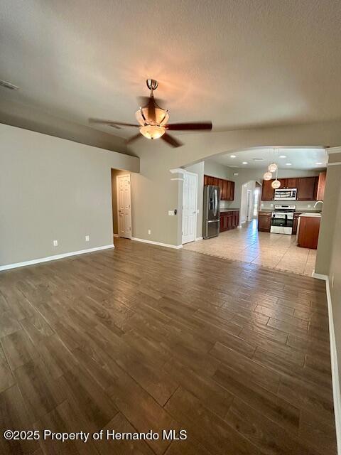 unfurnished living room featuring baseboards, a ceiling fan, arched walkways, and wood finished floors