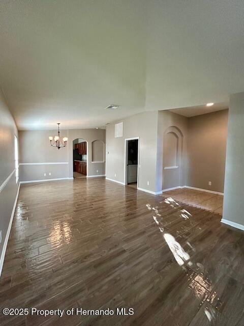 unfurnished living room with a chandelier, arched walkways, baseboards, and wood finished floors