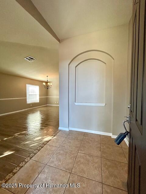 tiled spare room featuring baseboards, visible vents, and an inviting chandelier