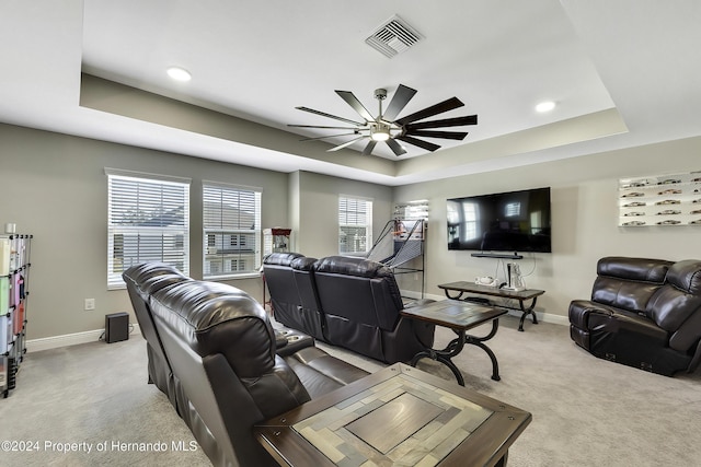 living room with a raised ceiling, light carpet, and ceiling fan