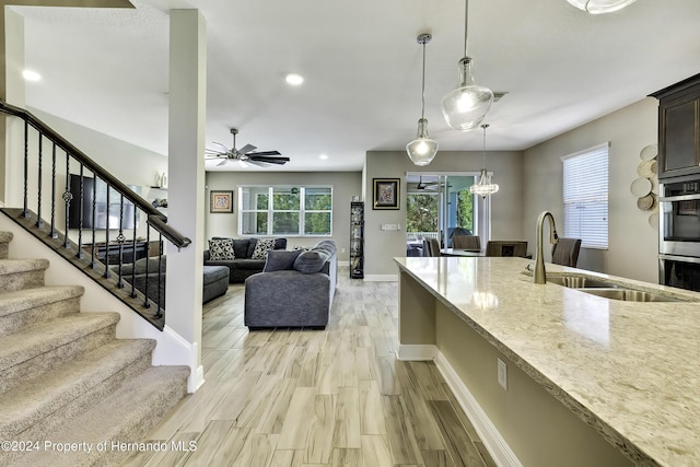 kitchen with pendant lighting, sink, ceiling fan, light wood-type flooring, and light stone countertops