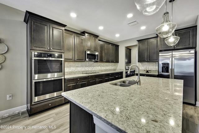 kitchen with sink, decorative backsplash, an island with sink, light stone counters, and stainless steel appliances