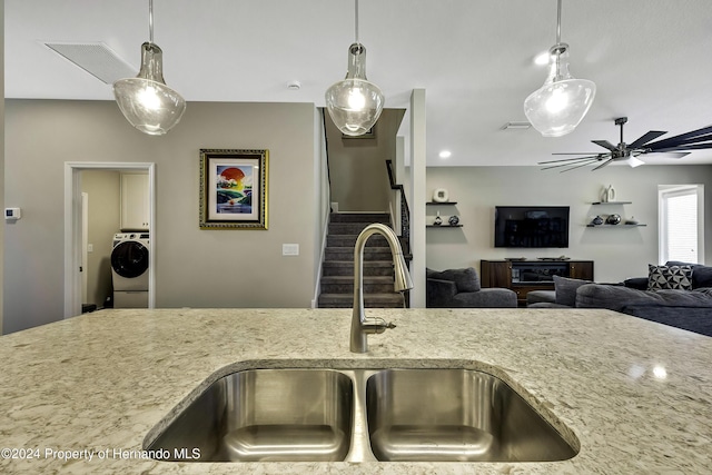 kitchen with light stone countertops, decorative light fixtures, washer / clothes dryer, and sink