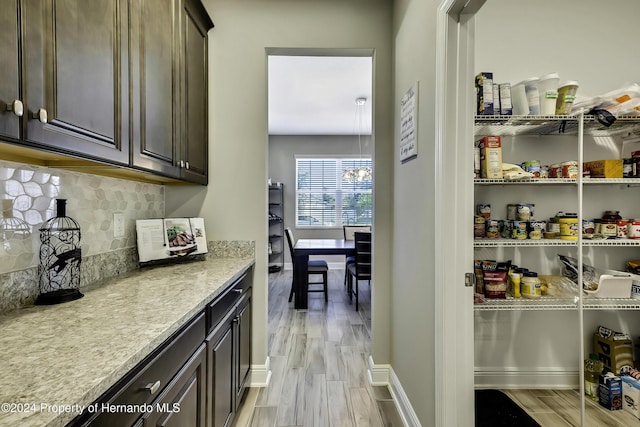 bar featuring decorative backsplash, dark brown cabinets, light hardwood / wood-style floors, and light stone countertops