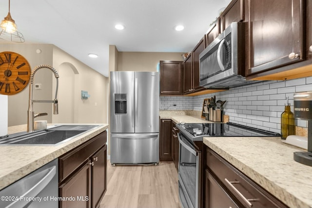 kitchen with sink, stainless steel appliances, backsplash, decorative light fixtures, and light wood-type flooring