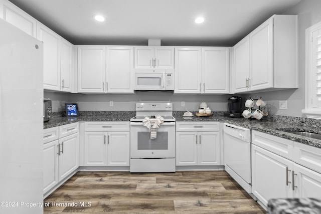 kitchen with white appliances, dark wood-type flooring, dark stone counters, sink, and white cabinetry