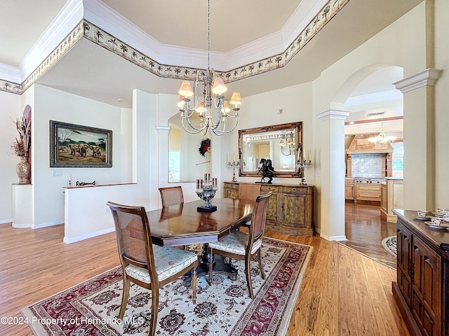 dining room featuring a notable chandelier, ornate columns, crown molding, and light hardwood / wood-style flooring