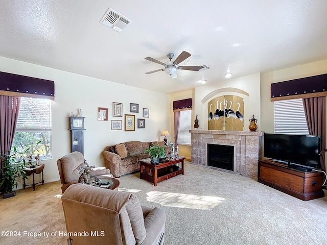 living room with a tile fireplace, ceiling fan, light colored carpet, and a textured ceiling