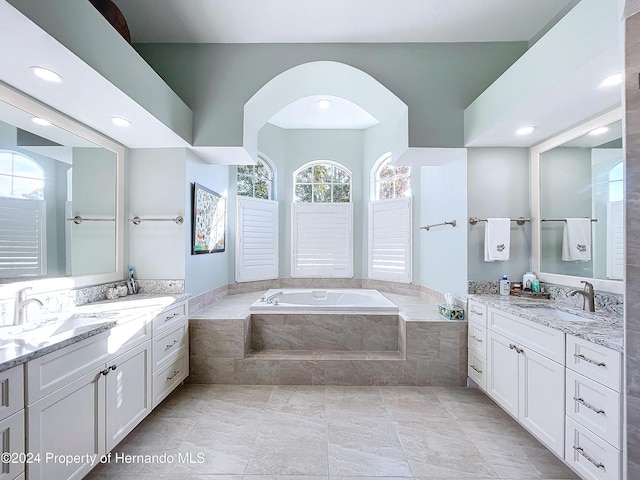 bathroom with tile patterned flooring, plenty of natural light, vanity, and tiled bath