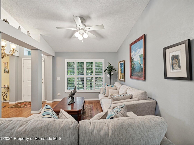 living room with hardwood / wood-style floors, ceiling fan with notable chandelier, lofted ceiling, and a textured ceiling