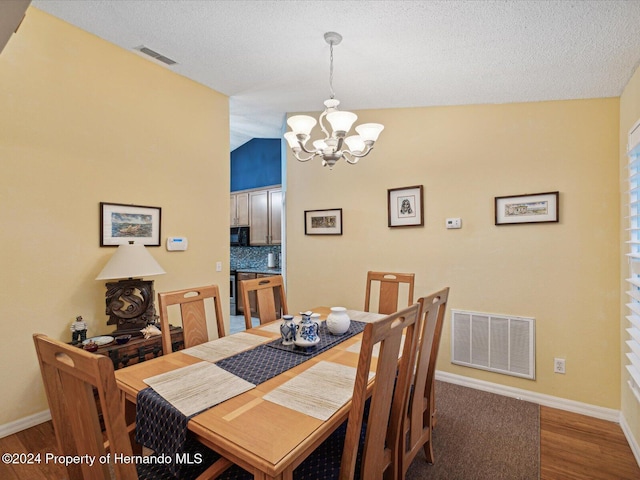 dining space featuring an inviting chandelier, wood-type flooring, a textured ceiling, and vaulted ceiling