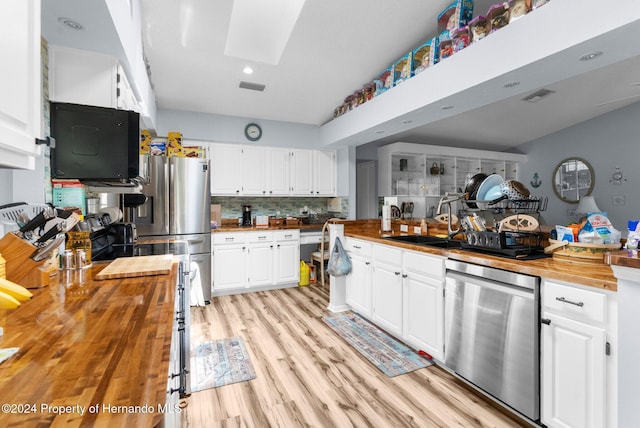 kitchen featuring lofted ceiling with skylight, white cabinets, stainless steel appliances, and wood counters