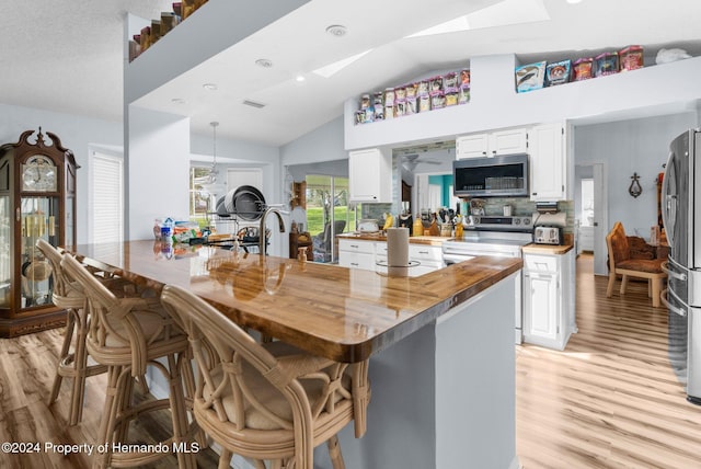 kitchen featuring white cabinets, wood counters, stainless steel appliances, and vaulted ceiling