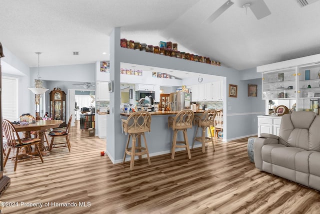 living room with ceiling fan, high vaulted ceiling, light hardwood / wood-style floors, and a textured ceiling