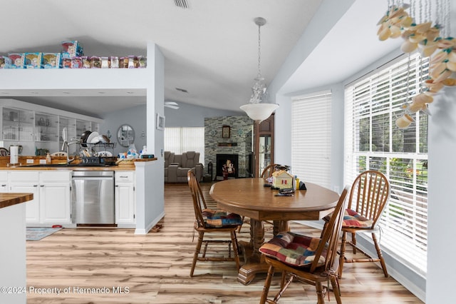 dining area with plenty of natural light, a stone fireplace, light hardwood / wood-style flooring, and vaulted ceiling