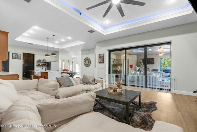 living room with ceiling fan, a raised ceiling, light hardwood / wood-style flooring, crown molding, and a textured ceiling