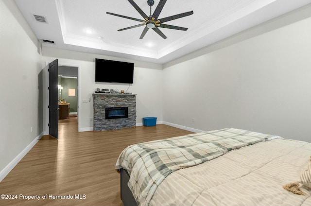 bedroom featuring hardwood / wood-style floors, ceiling fan, a stone fireplace, and a raised ceiling