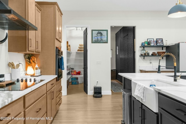 kitchen featuring pendant lighting, black appliances, wall chimney range hood, light hardwood / wood-style flooring, and light stone counters