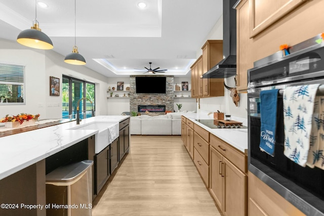 kitchen with sink, wall chimney exhaust hood, pendant lighting, a tray ceiling, and black appliances