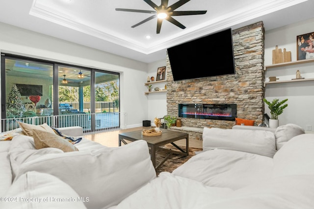 living room with a fireplace, a tray ceiling, ceiling fan, and ornamental molding