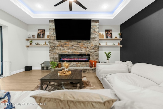 living room featuring a tray ceiling, a stone fireplace, ceiling fan, and ornamental molding