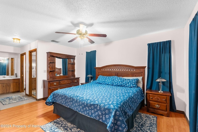 bedroom featuring a textured ceiling, light wood-type flooring, ensuite bathroom, and ceiling fan