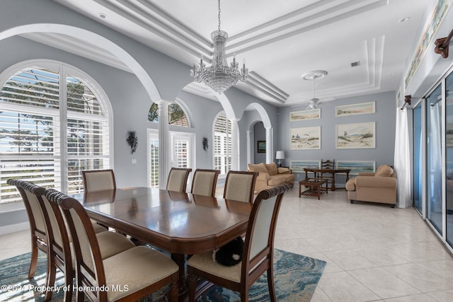 tiled dining room with ceiling fan with notable chandelier, a raised ceiling, ornate columns, and crown molding