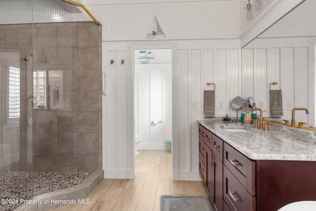 bathroom featuring a tile shower, vanity, wood-type flooring, and toilet