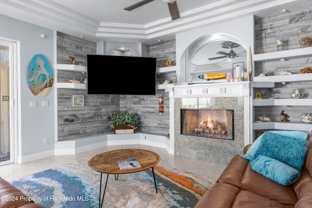 living room with ceiling fan, light tile patterned floors, a textured ceiling, a fireplace, and a tray ceiling