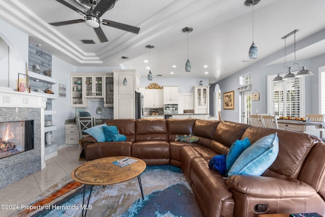 tiled living room featuring a high end fireplace, a textured ceiling, a tray ceiling, and ceiling fan